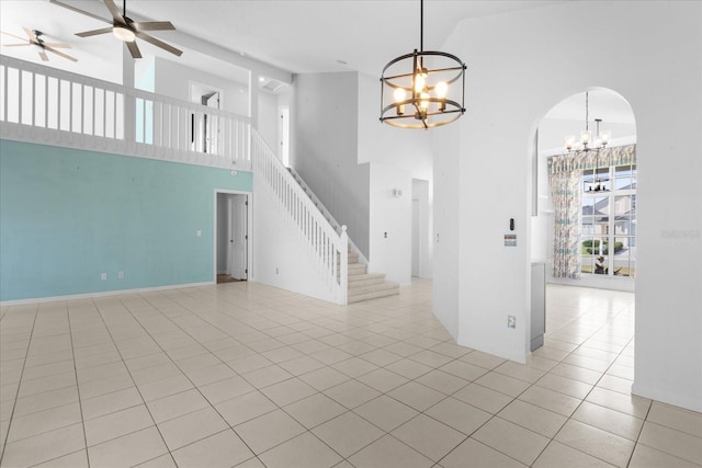 unfurnished living room featuring light tile patterned floors, stairs, arched walkways, and ceiling fan with notable chandelier