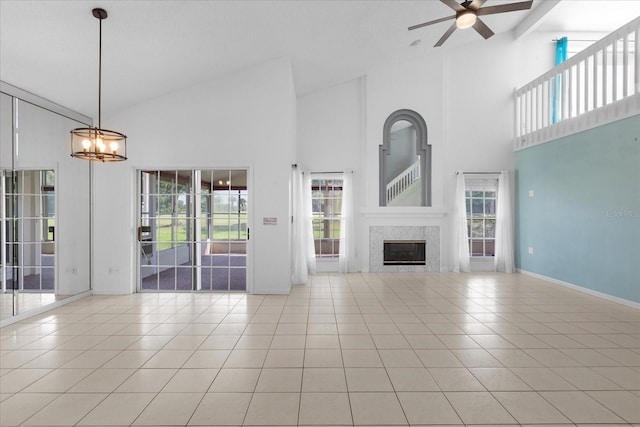 unfurnished living room featuring baseboards, light tile patterned flooring, a fireplace, high vaulted ceiling, and ceiling fan with notable chandelier