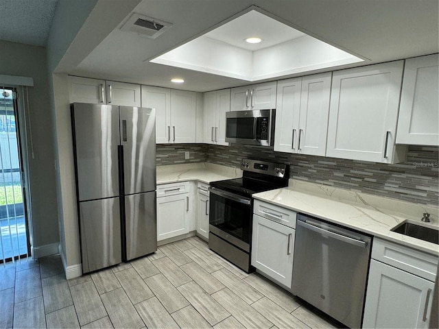 kitchen featuring sink, stainless steel appliances, light stone counters, backsplash, and white cabinets