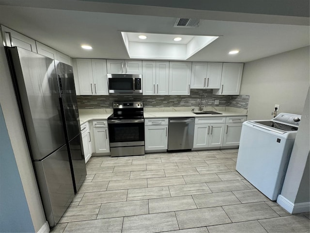 kitchen featuring sink, a tray ceiling, washer / dryer, white cabinetry, and stainless steel appliances