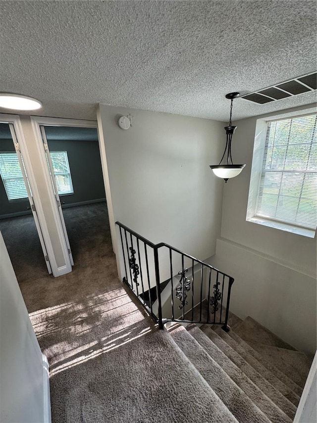 stairs featuring a textured ceiling and carpet floors