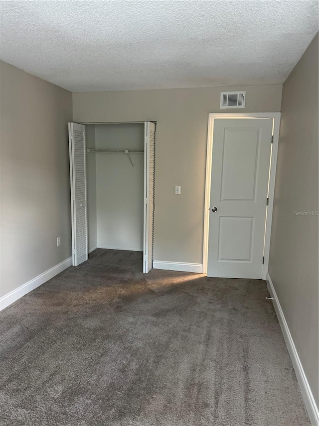 unfurnished bedroom featuring a textured ceiling, dark carpet, and a closet