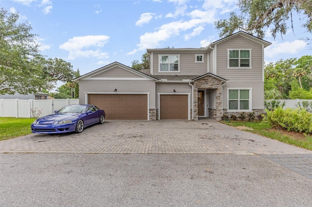 view of front of property with stone siding, decorative driveway, an attached garage, and fence