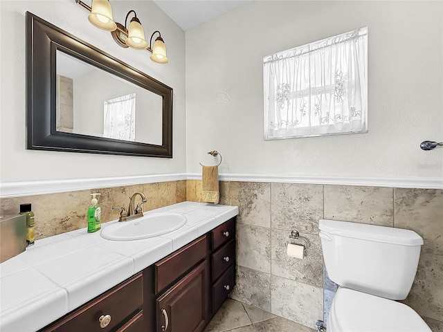 bathroom featuring tile flooring, vanity, toilet, and tile walls