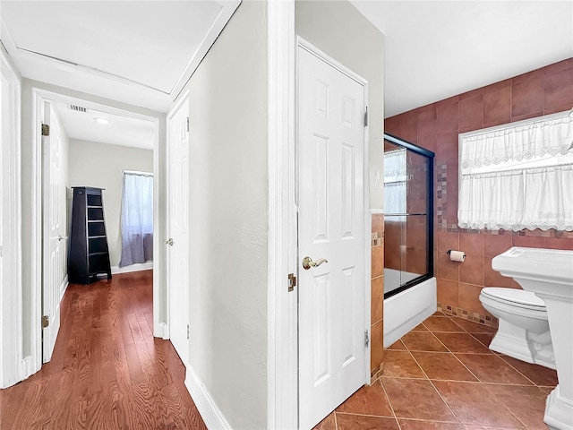 bathroom with tile walls, tile floors, enclosed tub / shower combo, and toilet