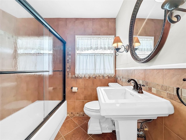 bathroom featuring tile floors, shower / bath combination with glass door, toilet, and tile walls