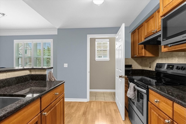 kitchen featuring stainless steel appliances, dark stone countertops, crown molding, decorative backsplash, and light wood-type flooring