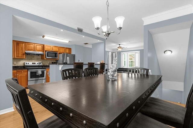 kitchen featuring decorative backsplash, appliances with stainless steel finishes, ceiling fan with notable chandelier, pendant lighting, and light hardwood / wood-style floors