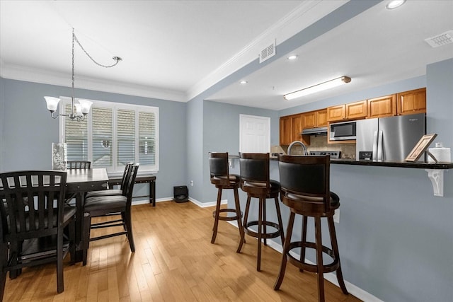 kitchen with appliances with stainless steel finishes, ornamental molding, pendant lighting, an inviting chandelier, and light hardwood / wood-style flooring