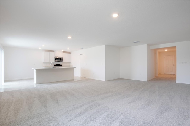 unfurnished living room featuring sink and light carpet