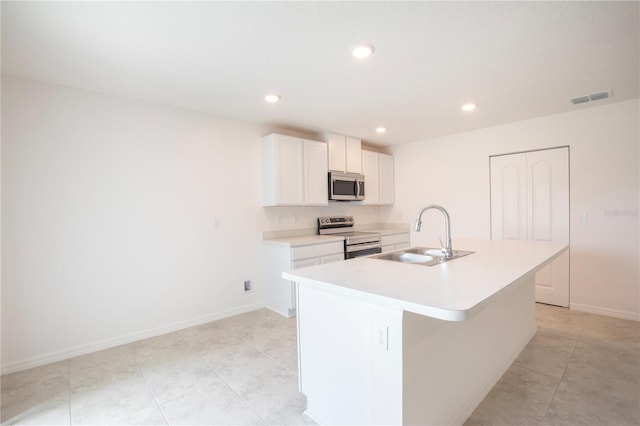 kitchen with light tile patterned floors, stainless steel appliances, a kitchen island with sink, white cabinets, and sink