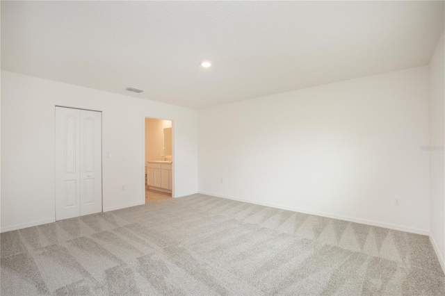 unfurnished bedroom with a closet, ensuite bathroom, and light colored carpet