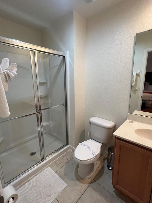 bathroom with tile floors, a shower with shower door, vanity, and toilet