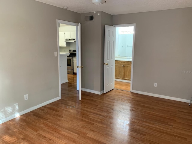 unfurnished bedroom with hardwood / wood-style floors, a walk in closet, and a textured ceiling