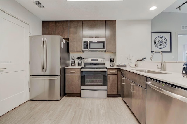 kitchen with dark brown cabinets, sink, light wood-type flooring, and appliances with stainless steel finishes