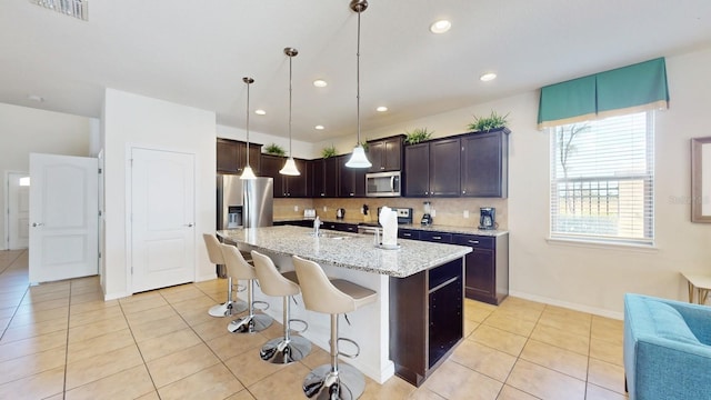 kitchen with a kitchen island with sink, light tile floors, backsplash, and appliances with stainless steel finishes