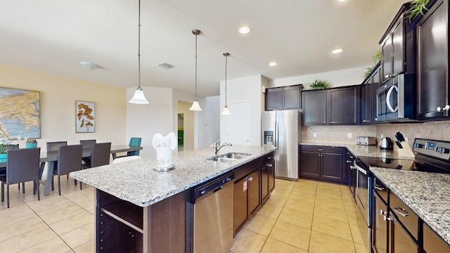 kitchen featuring stainless steel appliances, backsplash, a sink, light tile patterned flooring, and a center island with sink