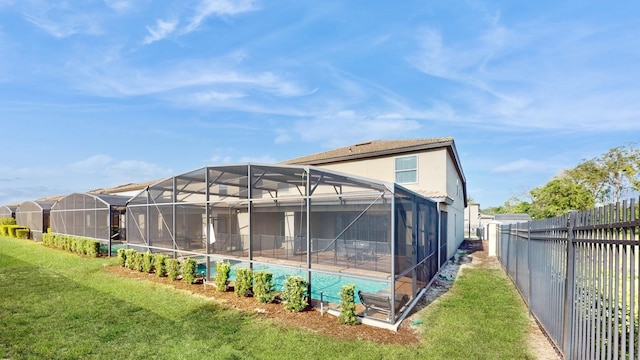 rear view of house featuring glass enclosure and a lawn