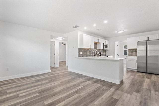 kitchen featuring stainless steel appliances, tasteful backsplash, light hardwood / wood-style flooring, kitchen peninsula, and white cabinets