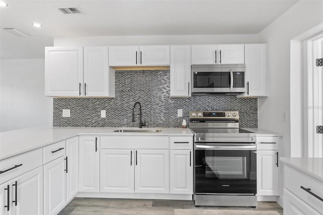 kitchen featuring decorative backsplash, stainless steel appliances, sink, light hardwood / wood-style flooring, and white cabinetry