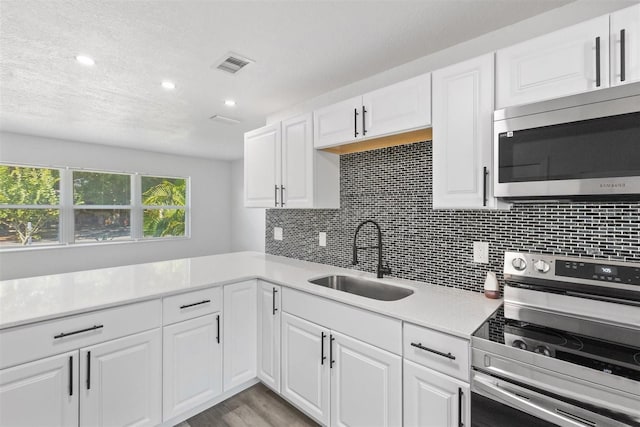 kitchen with sink, stainless steel appliances, backsplash, light hardwood / wood-style floors, and white cabinets