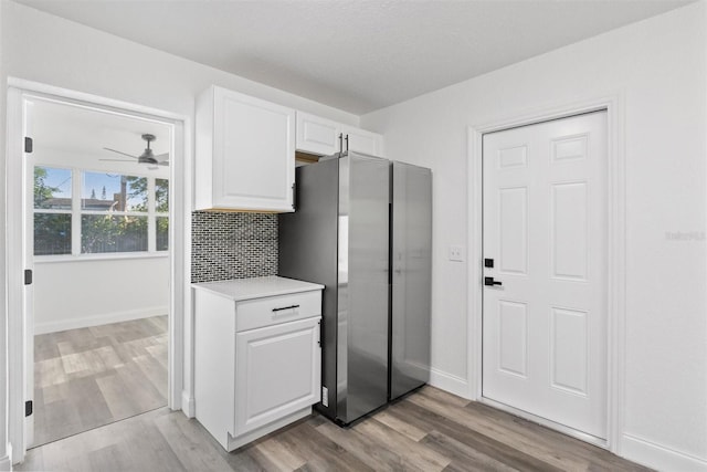 kitchen with backsplash, ceiling fan, light wood-type flooring, white cabinetry, and stainless steel refrigerator