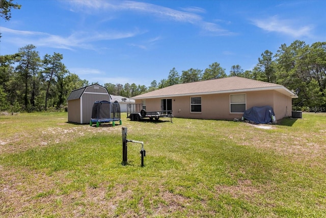 back of property featuring a trampoline, cooling unit, a yard, and a storage unit