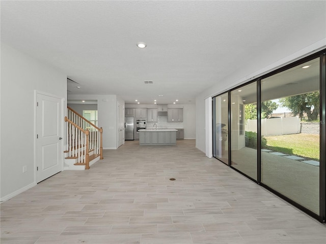 unfurnished living room with a textured ceiling, light hardwood / wood-style floors, and sink