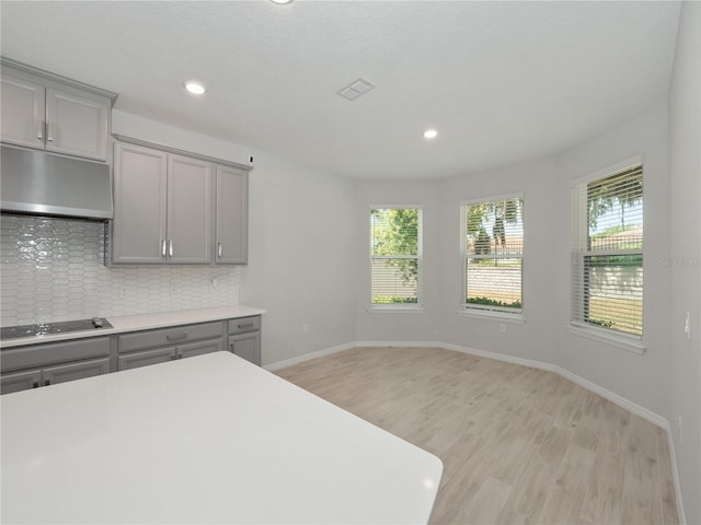 kitchen with gray cabinetry, decorative backsplash, black stovetop, and light hardwood / wood-style flooring