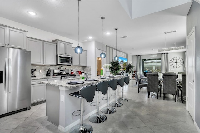 kitchen with stainless steel appliances, an island with sink, a breakfast bar area, decorative light fixtures, and light tile flooring