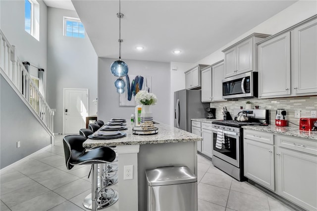 kitchen with a breakfast bar, light tile patterned floors, appliances with stainless steel finishes, pendant lighting, and light stone countertops