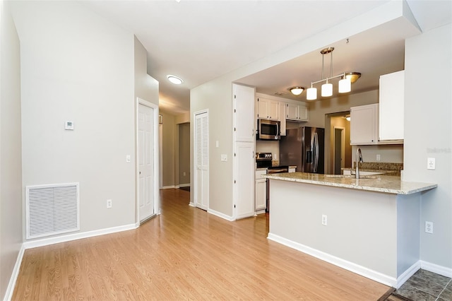 kitchen with appliances with stainless steel finishes, light wood-type flooring, sink, decorative light fixtures, and white cabinets