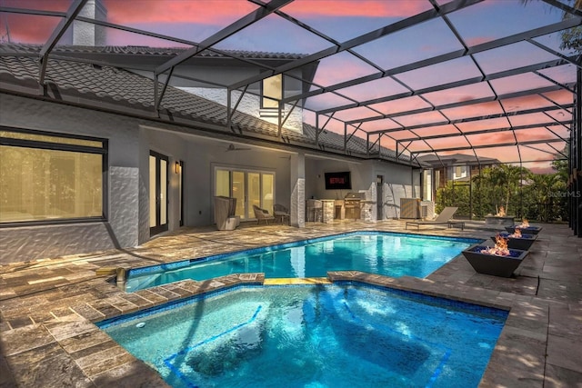 pool at dusk featuring an in ground hot tub, an outdoor kitchen, glass enclosure, and a patio area