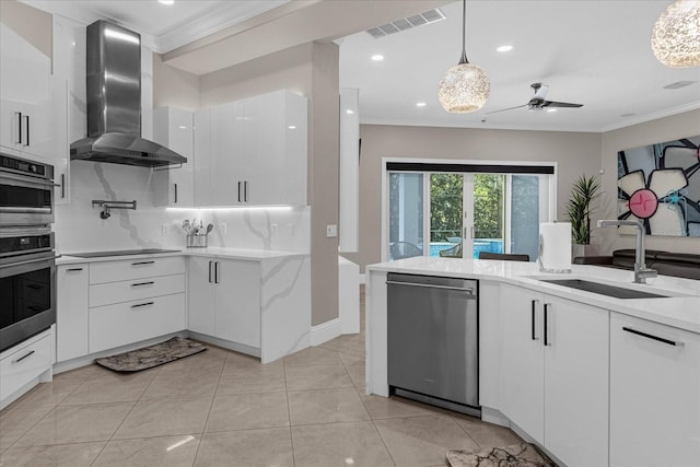 kitchen featuring wall chimney exhaust hood, sink, decorative light fixtures, stainless steel appliances, and white cabinets