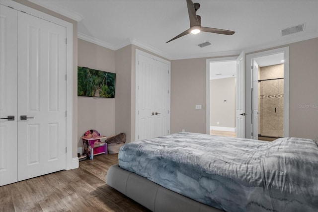 bedroom featuring ceiling fan, wood-type flooring, ornamental molding, and multiple closets