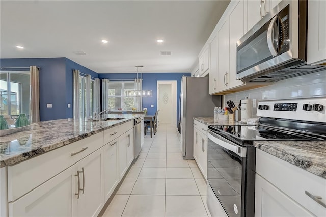 kitchen with appliances with stainless steel finishes, light stone counters, pendant lighting, an inviting chandelier, and white cabinetry