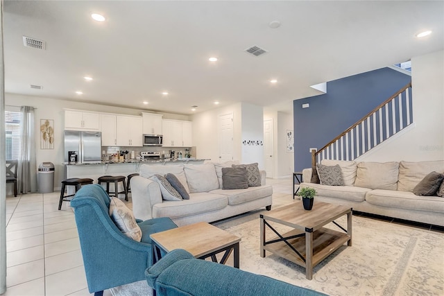 living room featuring light tile patterned floors, visible vents, recessed lighting, and stairs