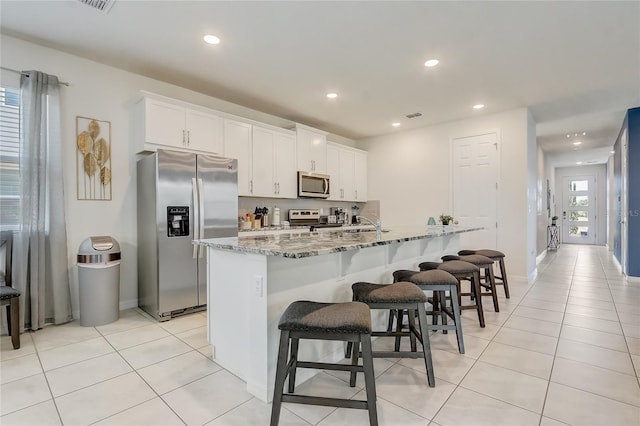 kitchen with an island with sink, appliances with stainless steel finishes, light stone counters, white cabinetry, and a breakfast bar area