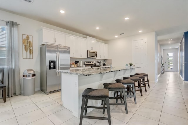 kitchen with a breakfast bar, light stone counters, light tile patterned floors, and appliances with stainless steel finishes