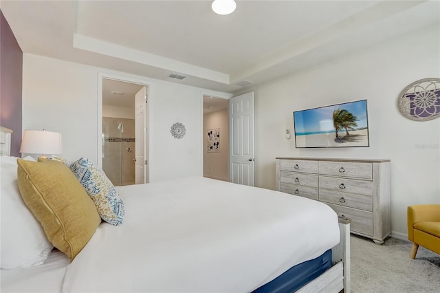 bedroom featuring a tray ceiling, ensuite bath, and light carpet