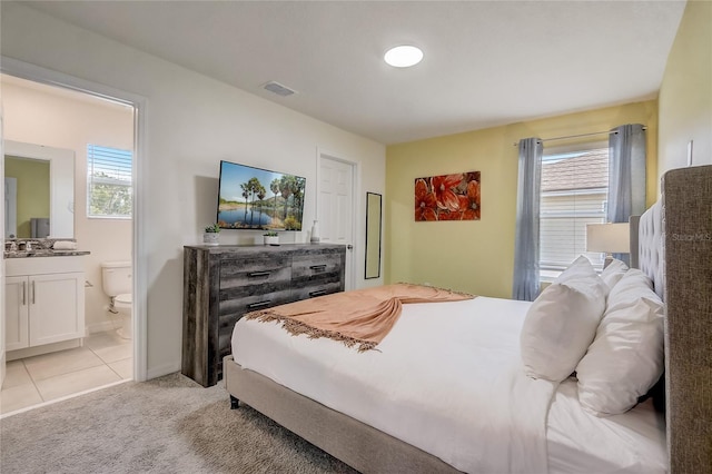 bedroom featuring visible vents, light carpet, ensuite bathroom, a sink, and light tile patterned flooring