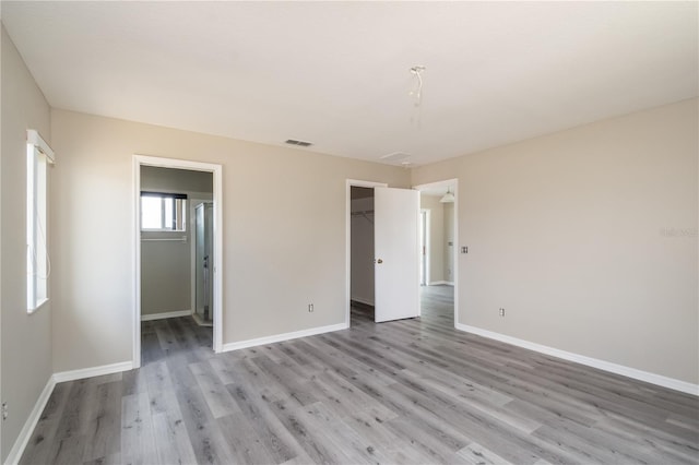 unfurnished bedroom featuring a walk in closet, light hardwood / wood-style flooring, and a closet