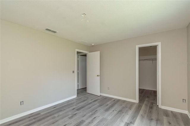 unfurnished bedroom featuring a spacious closet, a closet, and light hardwood / wood-style flooring