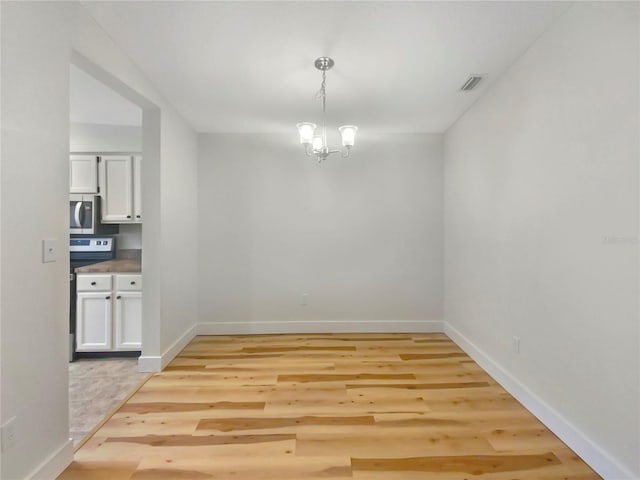 unfurnished dining area with a notable chandelier and light hardwood / wood-style flooring