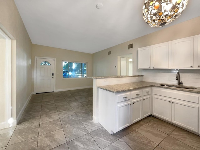 kitchen featuring white cabinetry, sink, light stone countertops, kitchen peninsula, and decorative backsplash