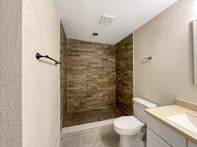 bathroom featuring vanity, tile patterned flooring, toilet, tiled shower, and a textured ceiling