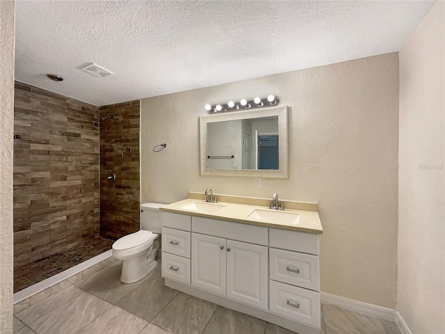 bathroom featuring a tile shower, vanity, a textured ceiling, and toilet