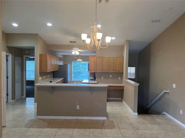 kitchen featuring a breakfast bar, hanging light fixtures, stainless steel refrigerator, kitchen peninsula, and ceiling fan with notable chandelier