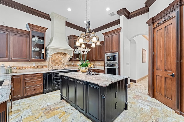 kitchen featuring decorative light fixtures, a center island, appliances with stainless steel finishes, custom range hood, and light stone countertops