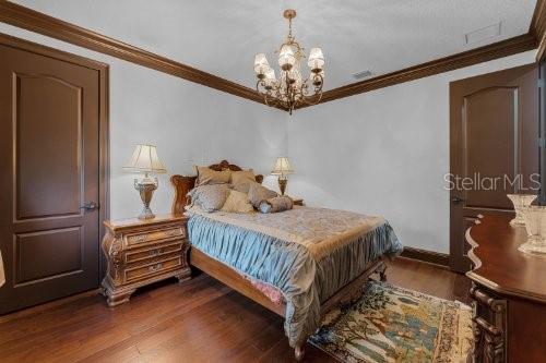 bedroom with dark hardwood / wood-style flooring, a notable chandelier, and ornamental molding